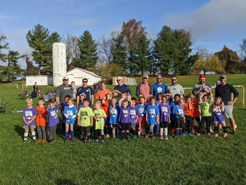 Youth soccer team and coaches posing on a grassy field near a large white monument.