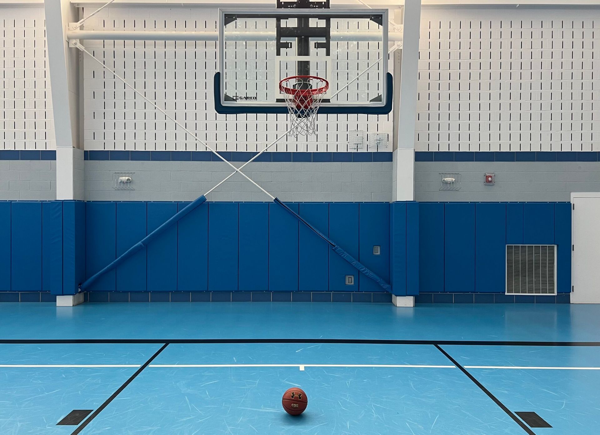 Empty indoor basketball court with a lone basketball near center court