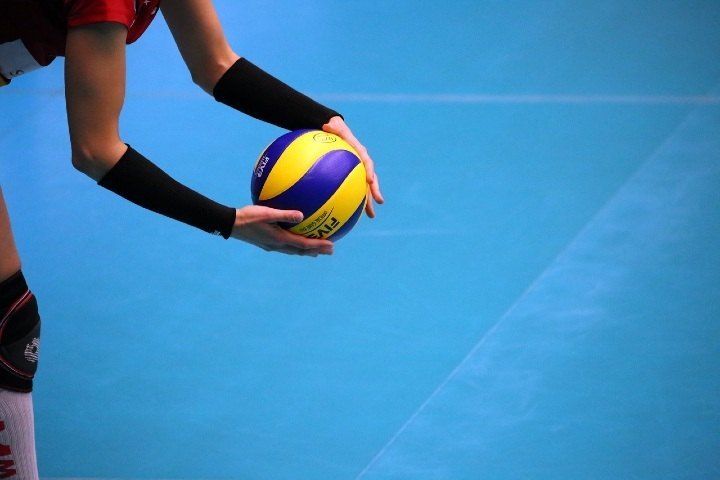 Volleyball player’s hands serving a yellow and blue ball on a blue court