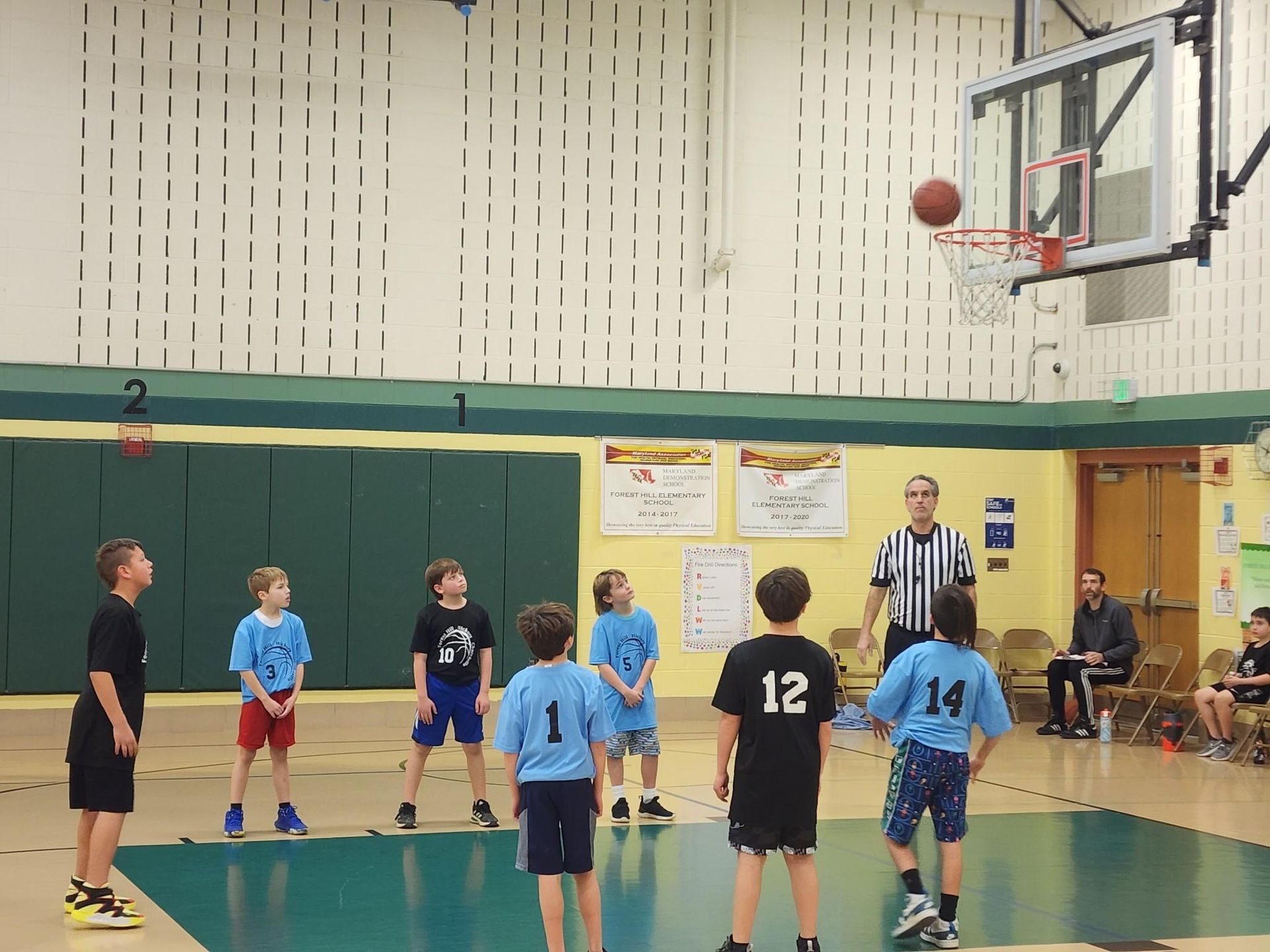 Youth basketball game in a gym, players under the hoop as the ball bounces off the rim.