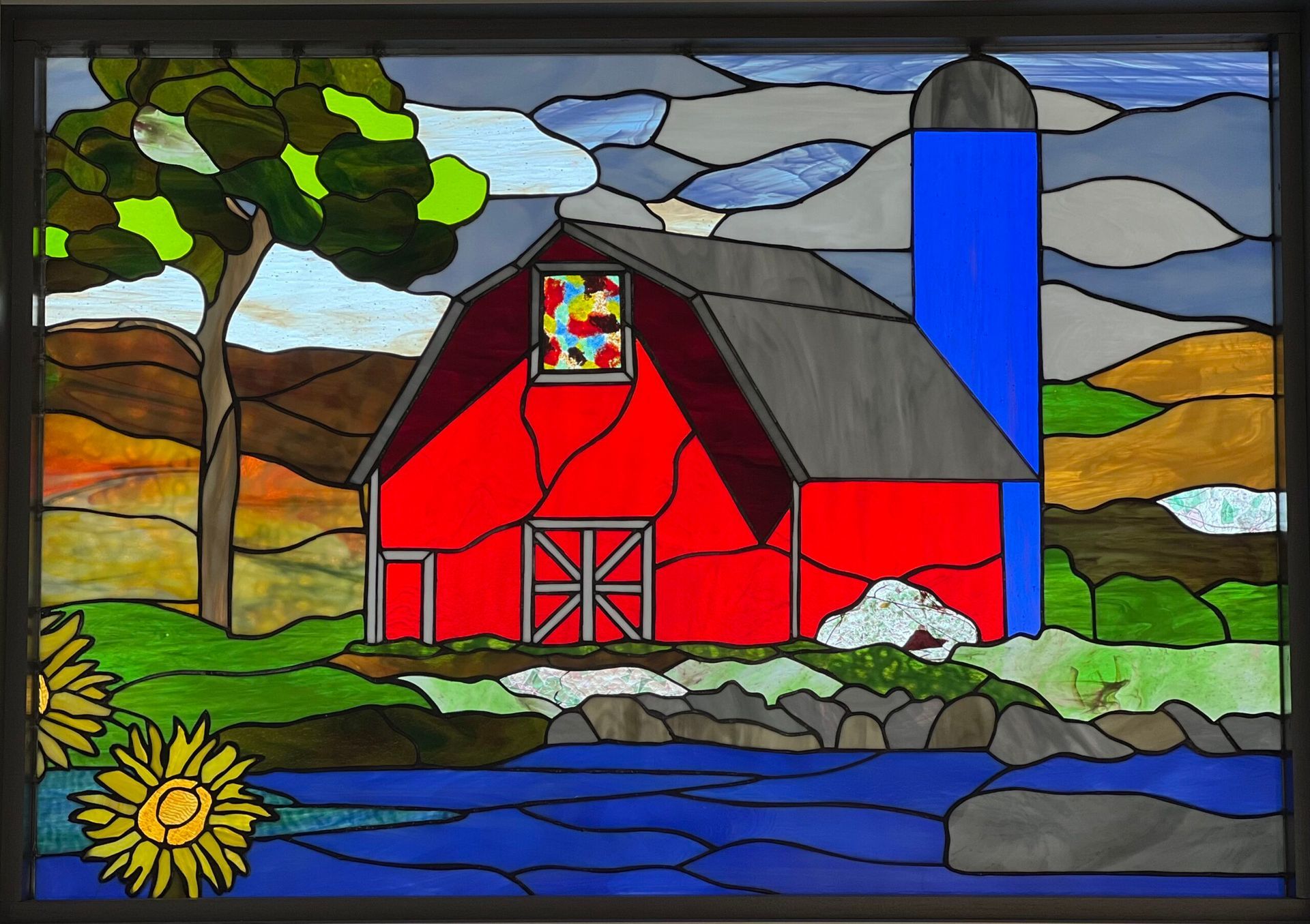 Stained-glass style red barn with blue silo, tree, water, and sun in a colorful rural landscape