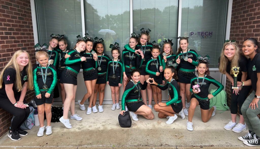 Youth sports team in black and green uniforms posing outside a building.