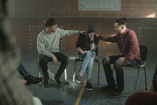 Two individuals consoling a man during group therapy. Group Therapy
