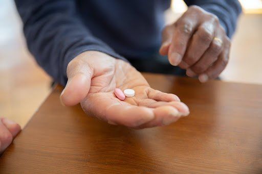 A person holding a white pill and a pink pill in their palm. Medication Assisted Treatment Program