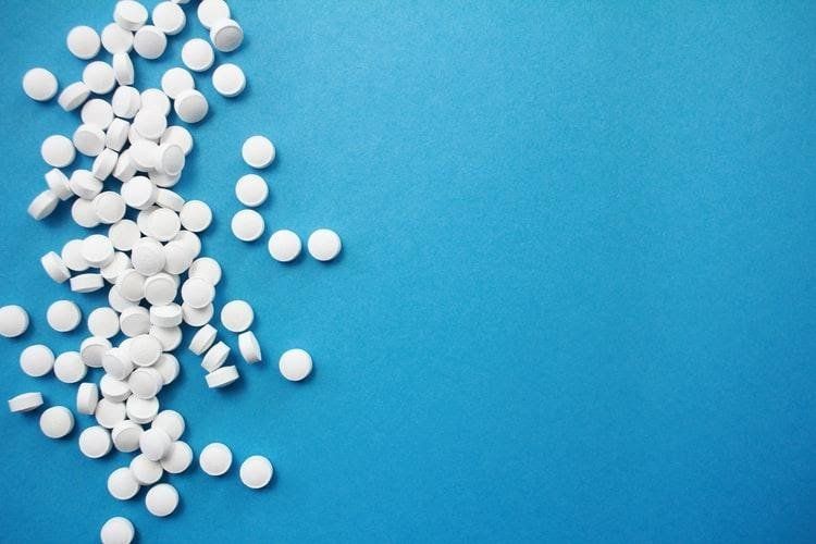 Round, white pills on a blue background. Symptoms of Oxycontin Abuse