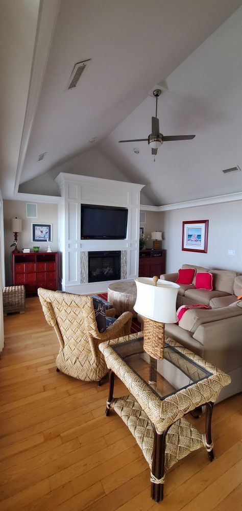 Bright living room with wicker chairs, beige sofa, ceiling fan, fireplace, and wall art