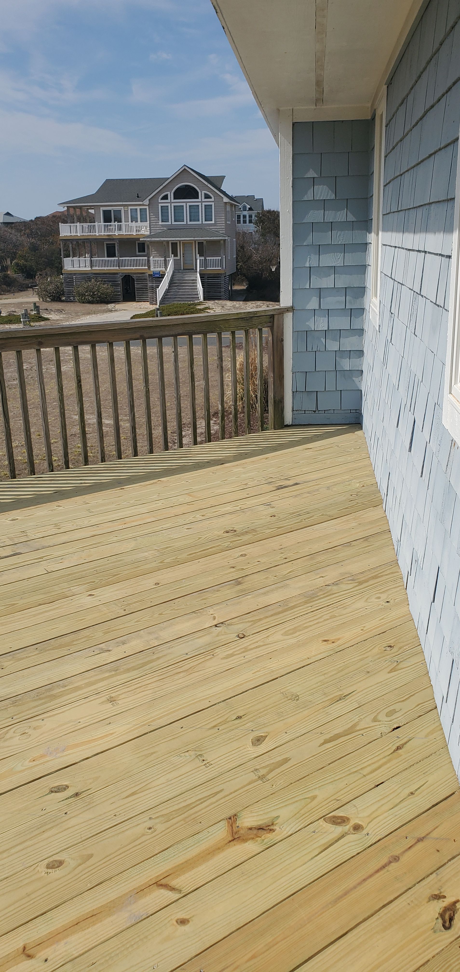 Wooden deck with railing and a blue house view across a yard