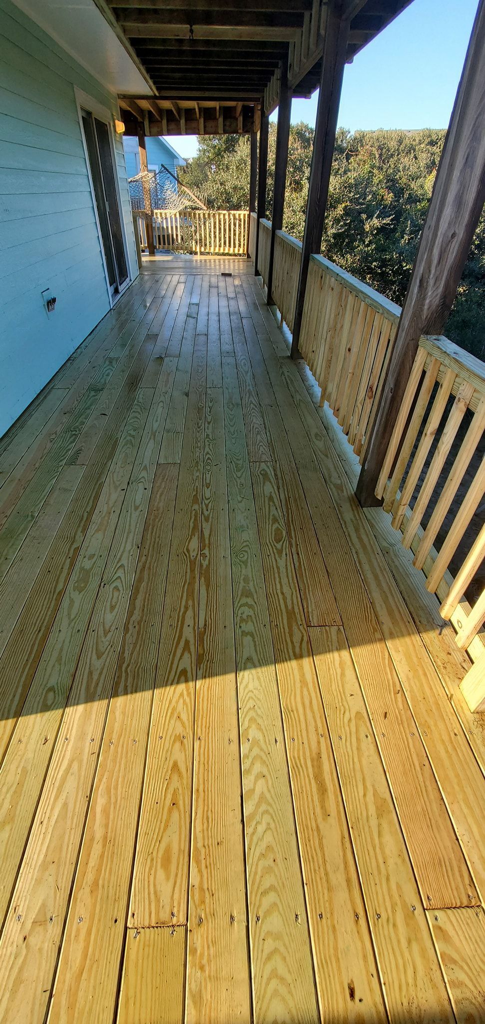Sunlit wooden porch with railings and snow-covered trees beyond