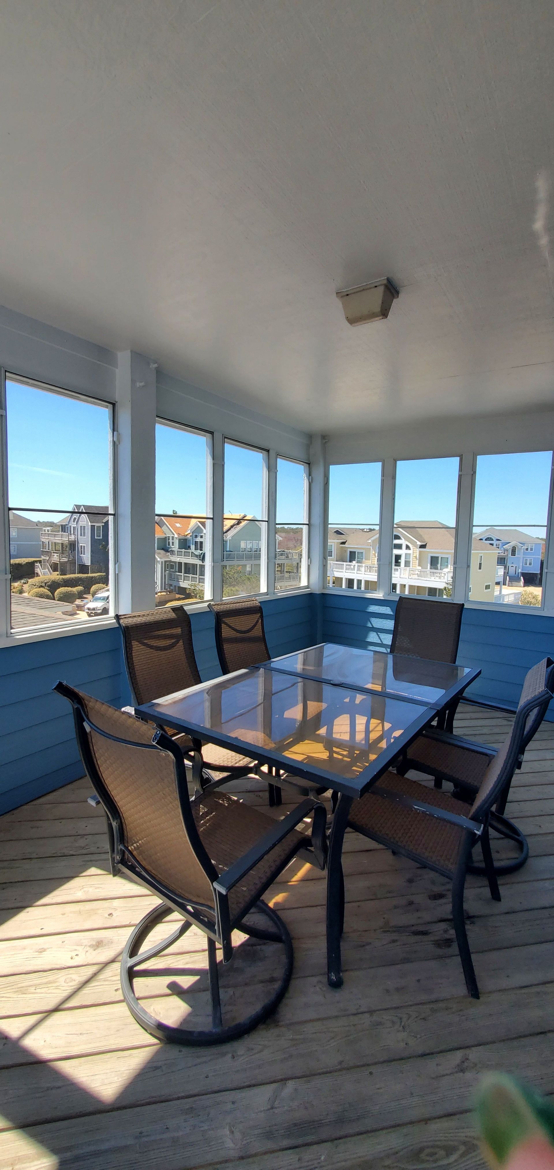 Covered patio with glass table and chairs overlooking a bright coastal view