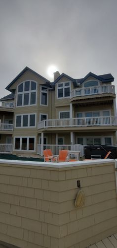 Beachfront condo building with balconies above a low wall and orange chairs under overcast skies