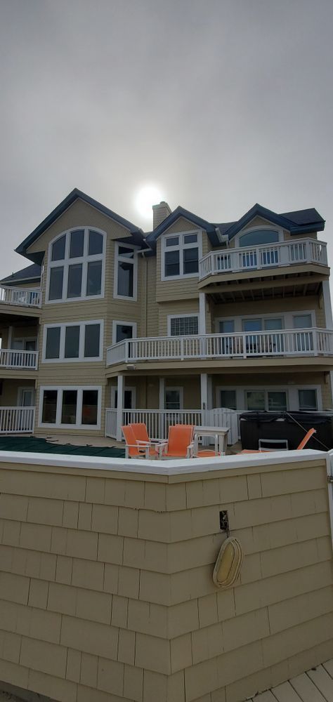 Large beach house with balconies behind a tan retaining wall under a cloudy sky.