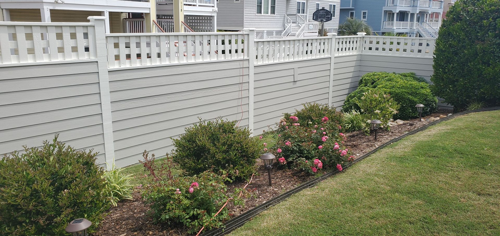 White lattice fence beside landscaped flower bed and green lawn near a waterfront walkway