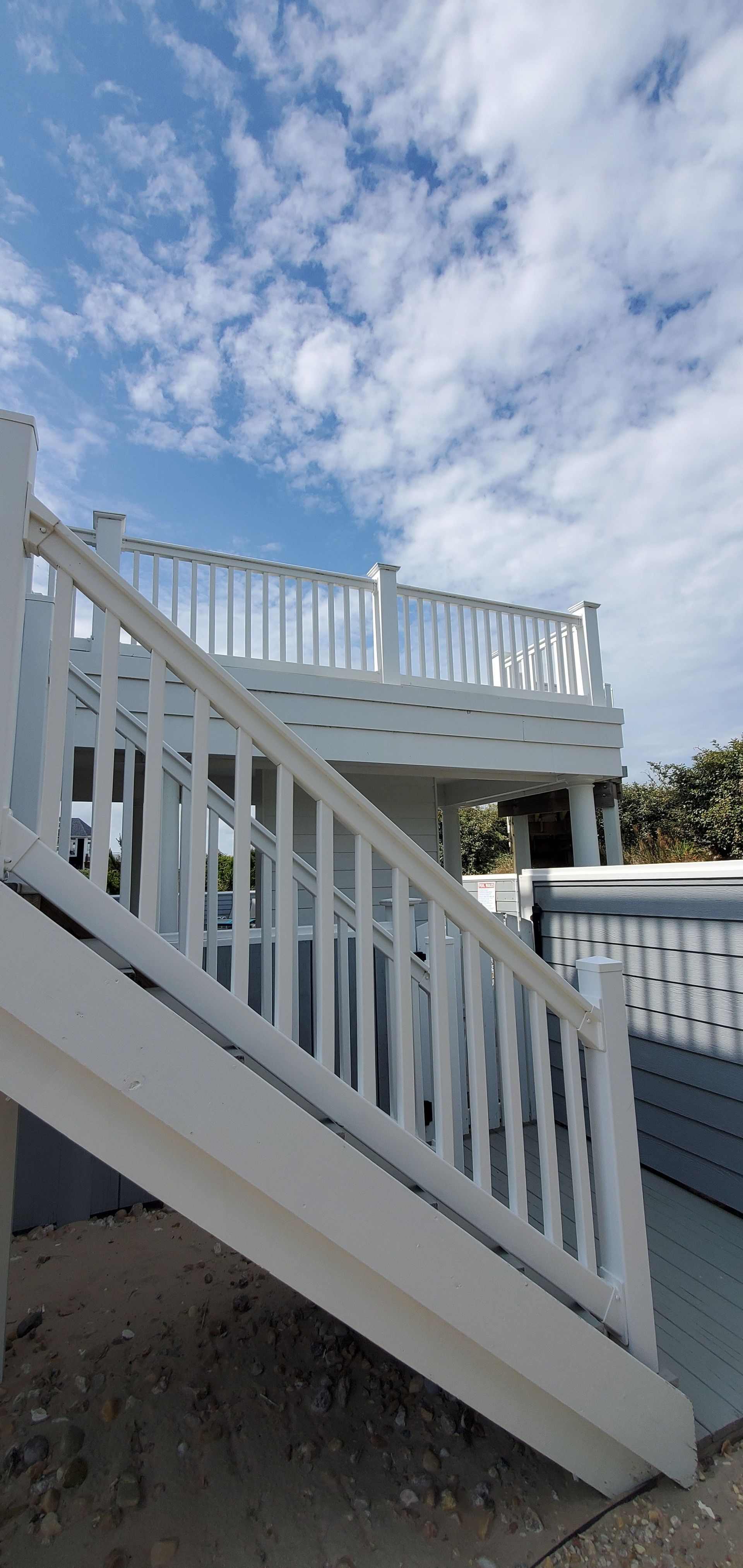 White outdoor staircase leading to a raised deck beneath a cloudy blue sky