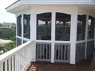 White screened porch with railings and wooden deck overlooking a landscape