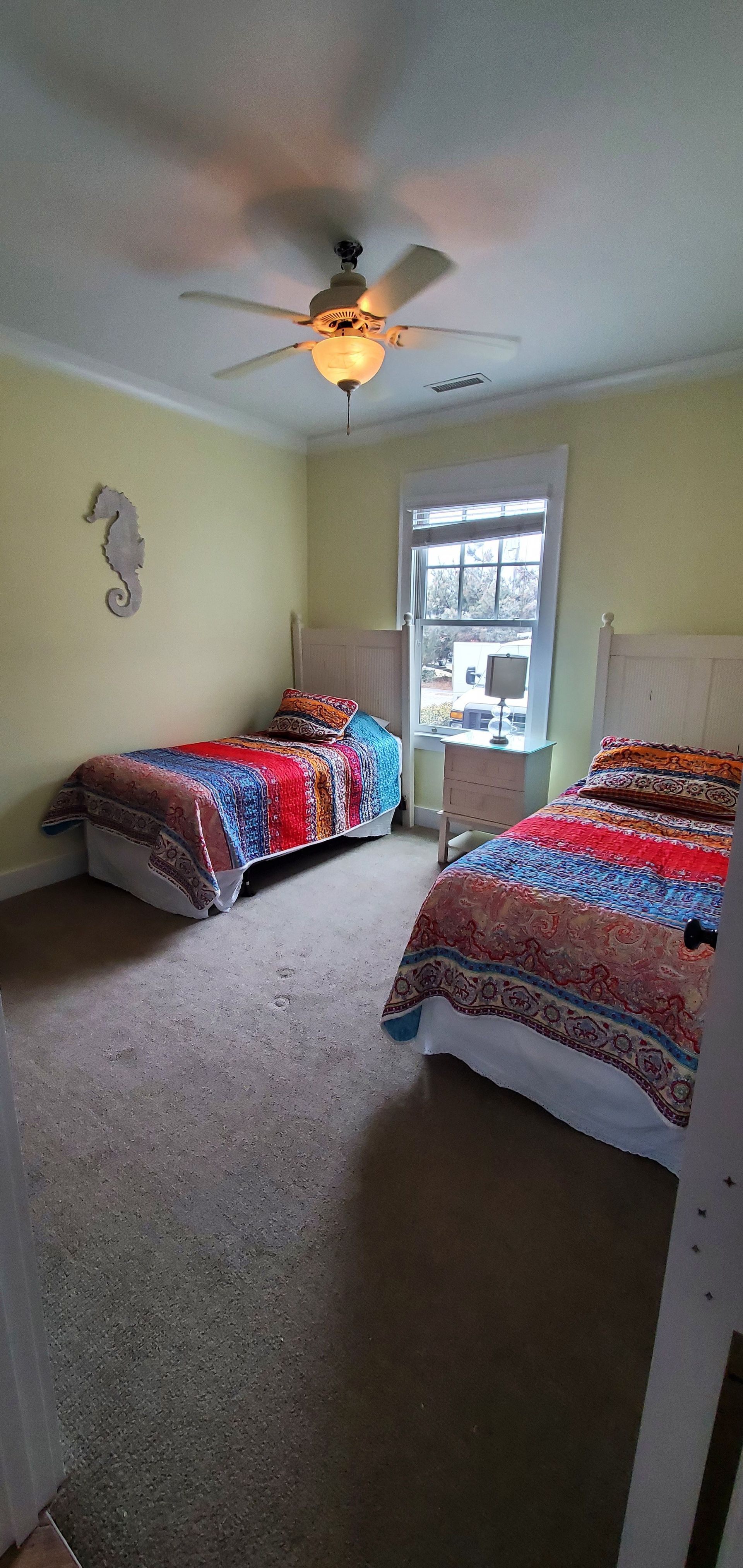Small bedroom with two beds, ceiling fan, window, and floral quilts in soft neutral tones