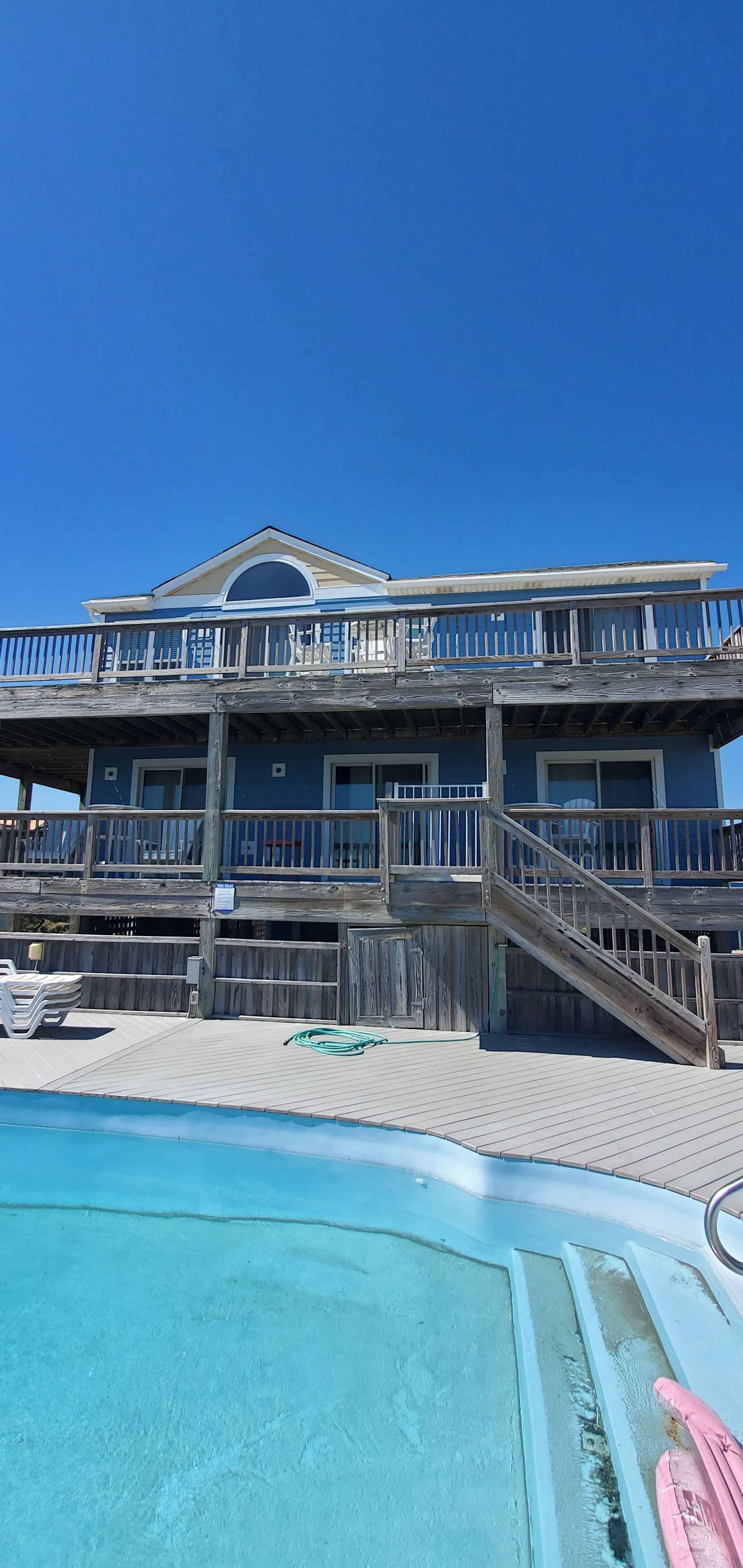 Blue pool in front of a weathered beach house under a clear sky