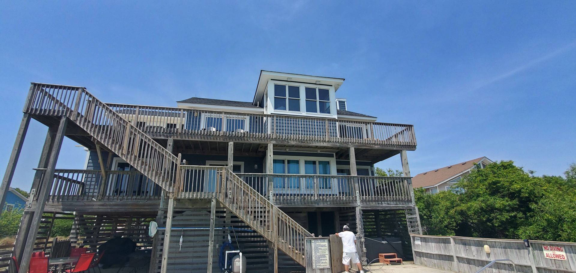Stilted beach house with blue railings and exterior stairs under a clear sky