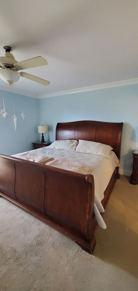 Bedroom with dark wood bed frame, white bedding, blue walls, and a ceiling fan.