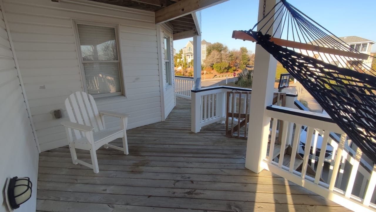 Porch with white rocking chairs, wooden floor, and a black hammock on a sunny day