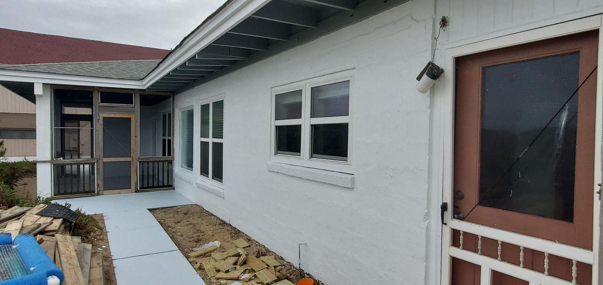 White house exterior with windows, red door, and a walkway under construction along the wall