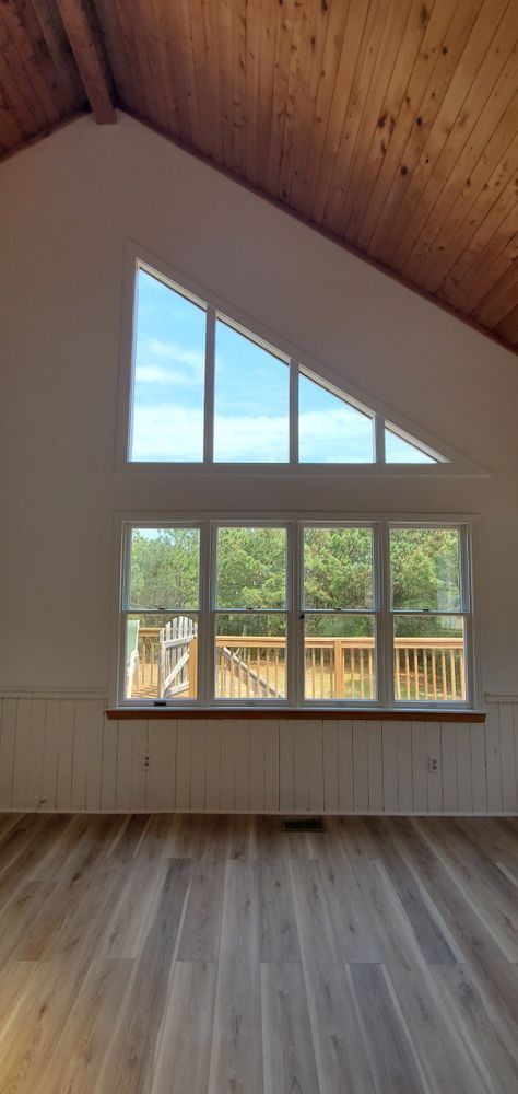 Vaulted wood-ceiling room with large triangular and rectangular windows overlooking a deck and trees