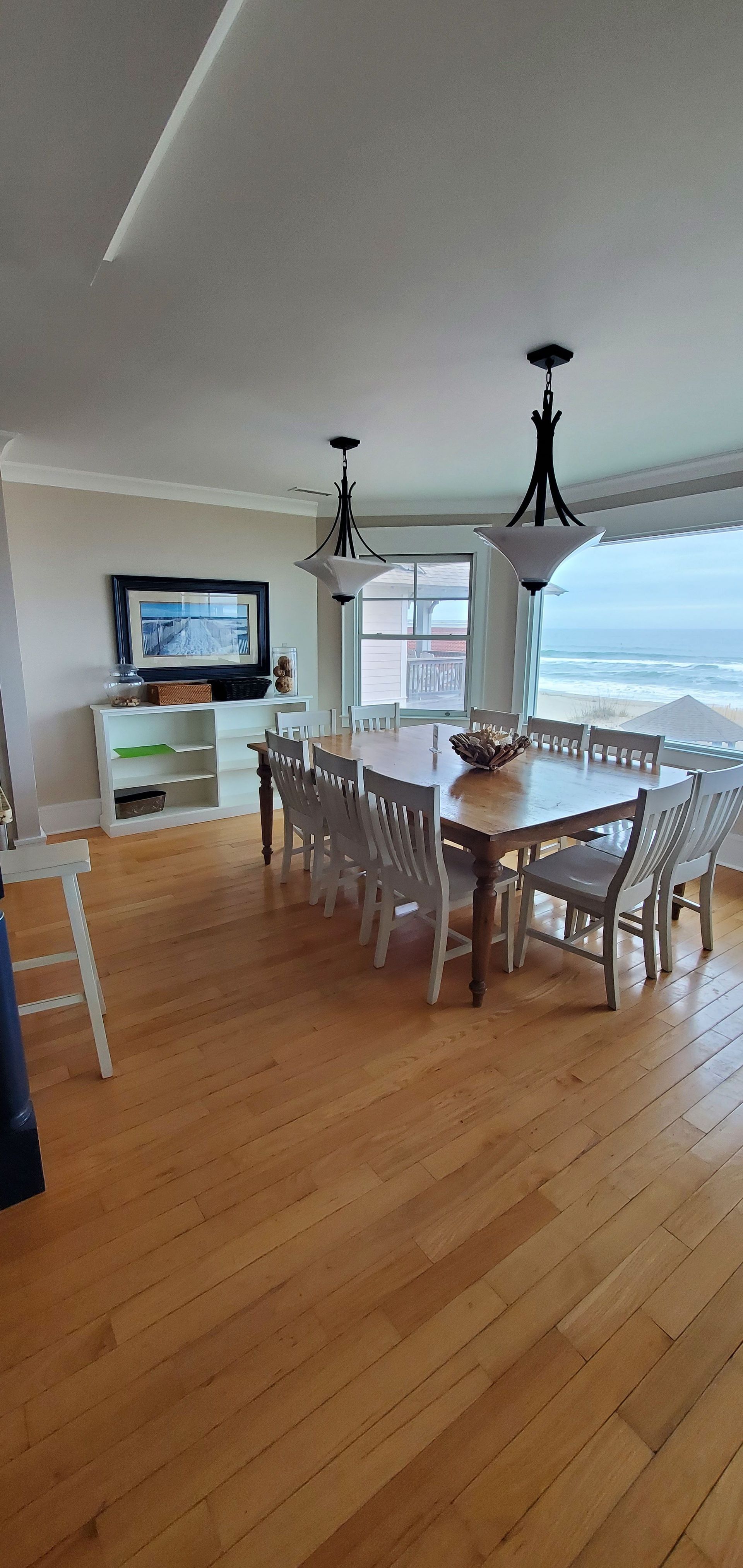 Bright dining room with wooden table, chairs, ocean-view window, and hardwood floors