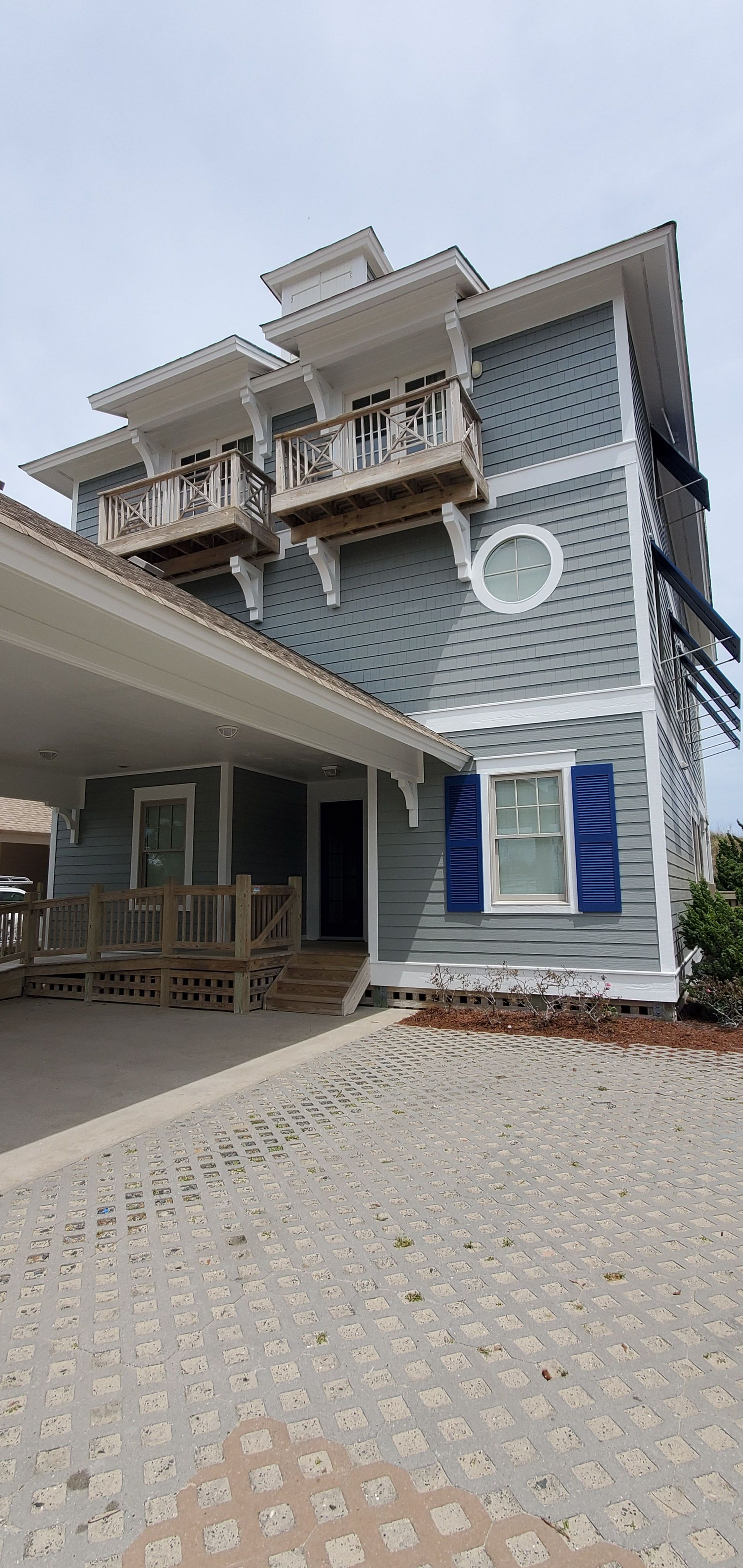 Two-story house with a covered porch, balcony, and tiled driveway under a cloudy sky