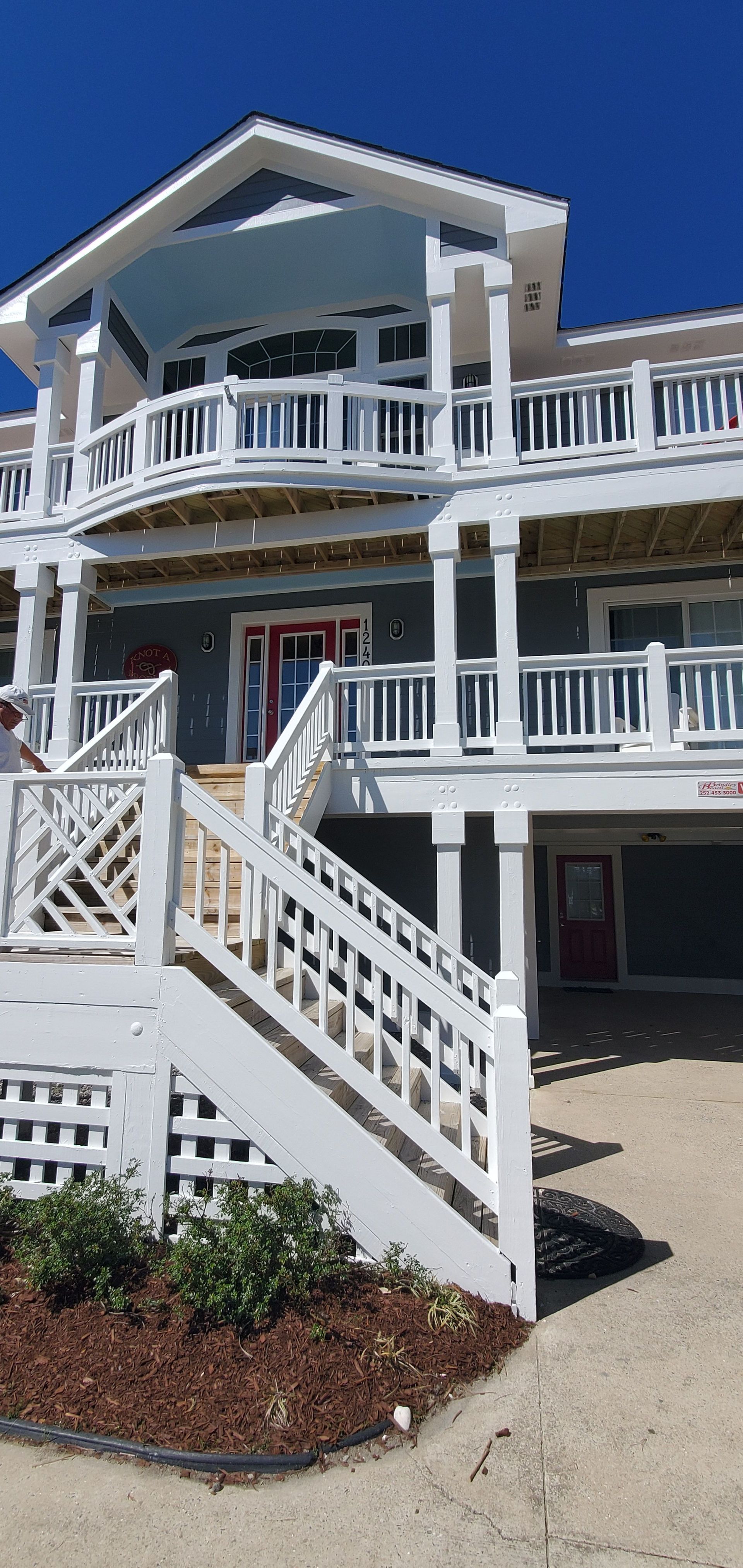 White coastal house with wraparound porch, staircase, and blue sky