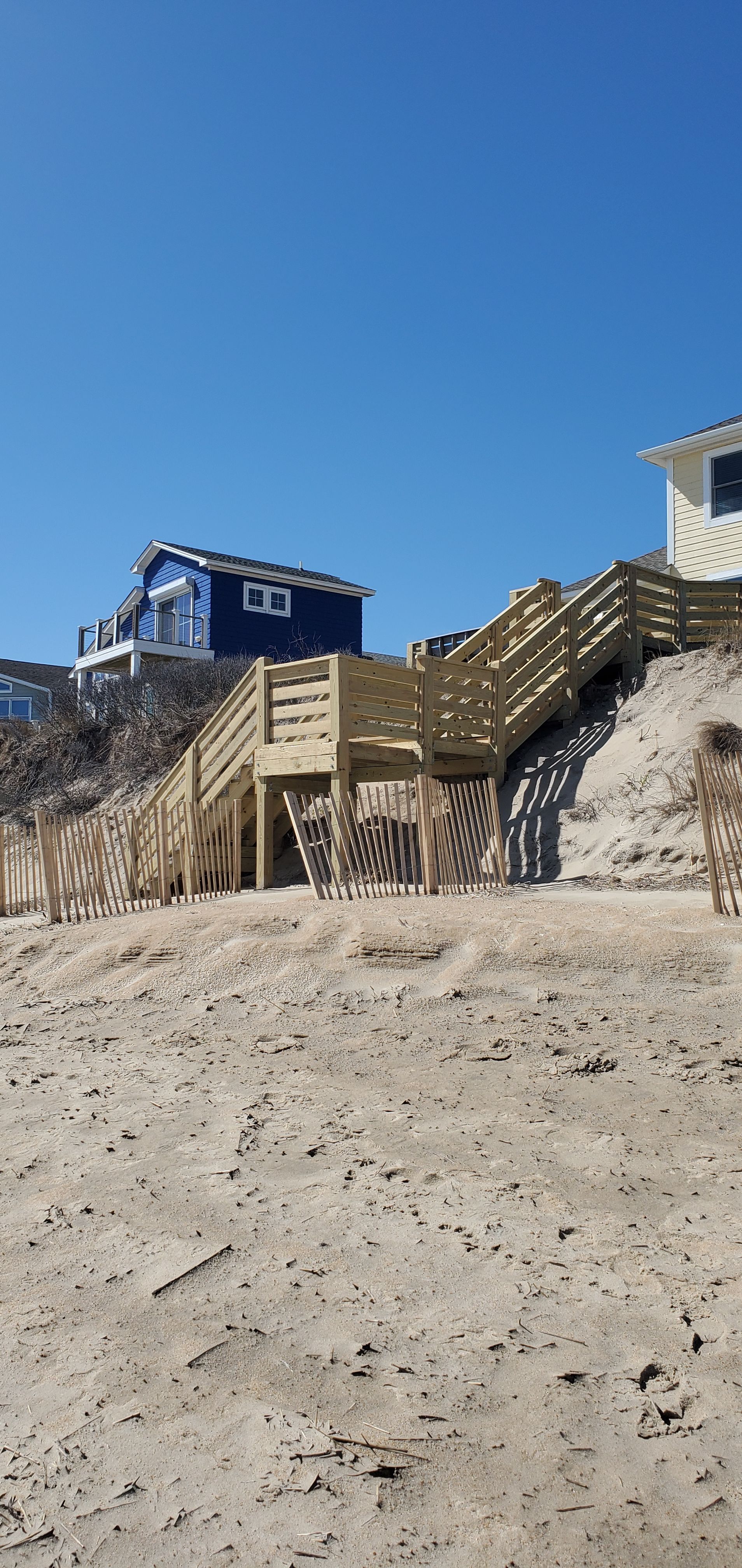 Beach access stairs beside dunes under a clear blue sky