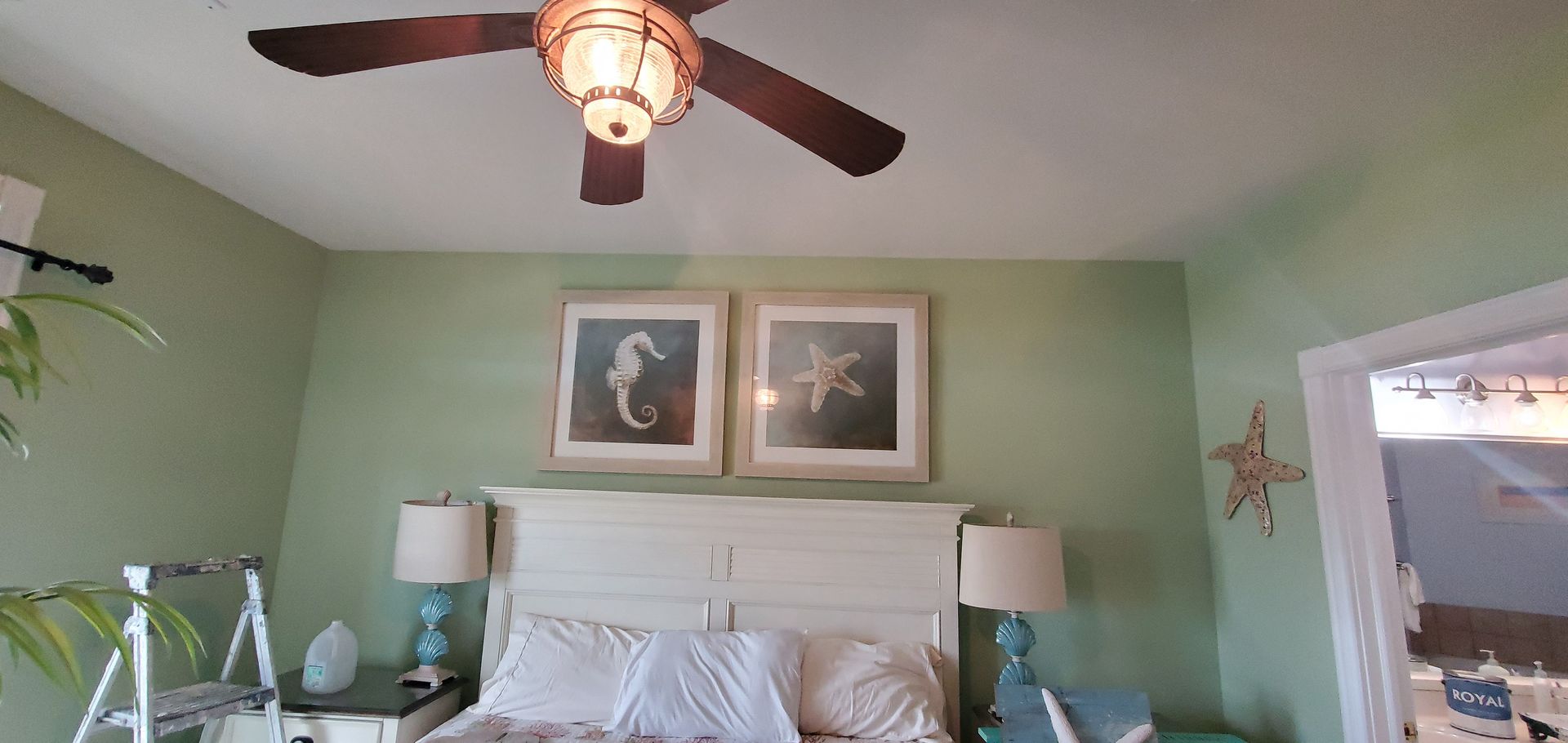 Bedroom with mint-green walls, white bed, ceiling fan, bedside lamps, and framed art above the headboard