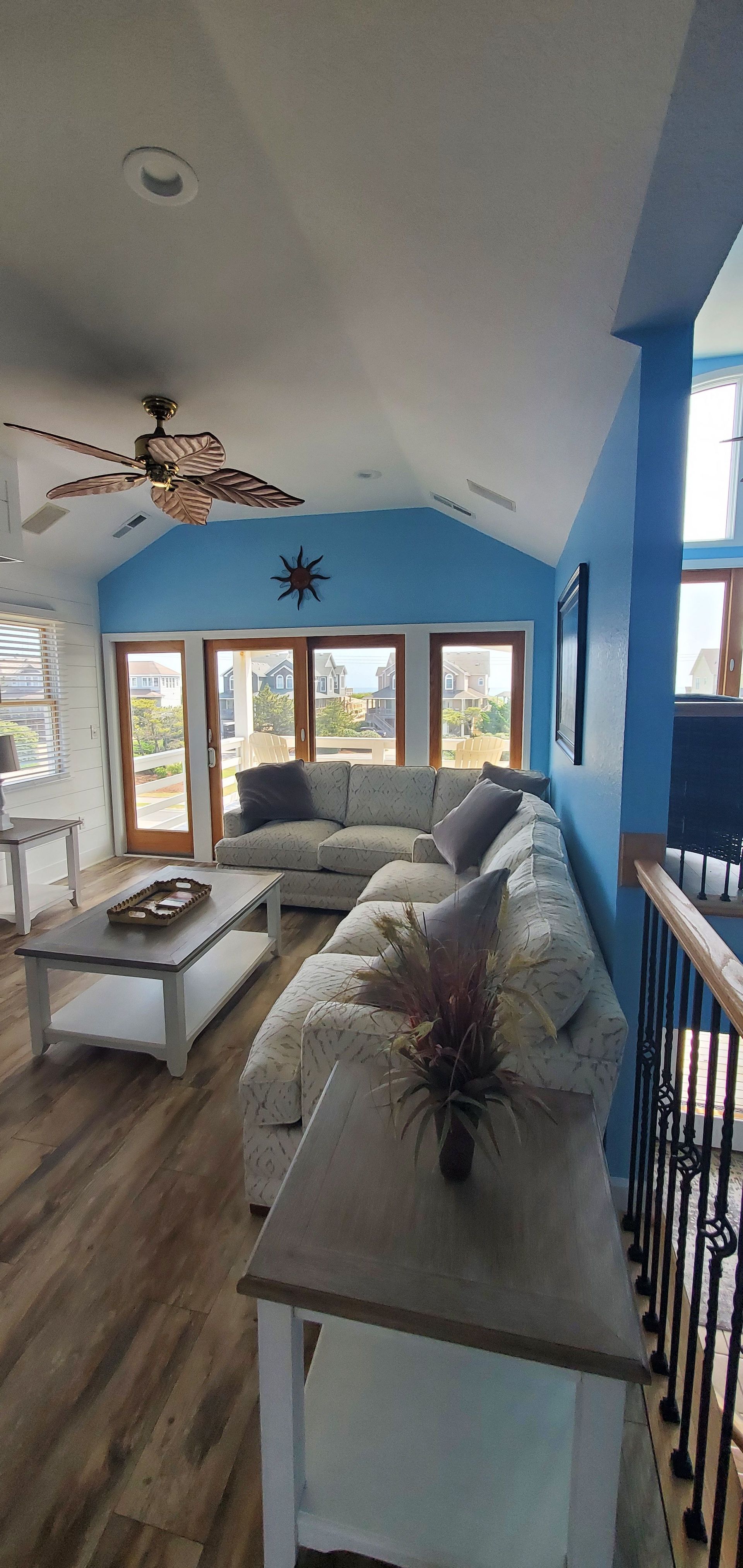 Bright living room with gray sofas, coffee table, hardwood floors, blue walls, and large windows.