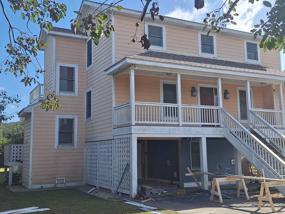 Two-story beige house with white porch railings, exterior stairs, and visible renovation work in front