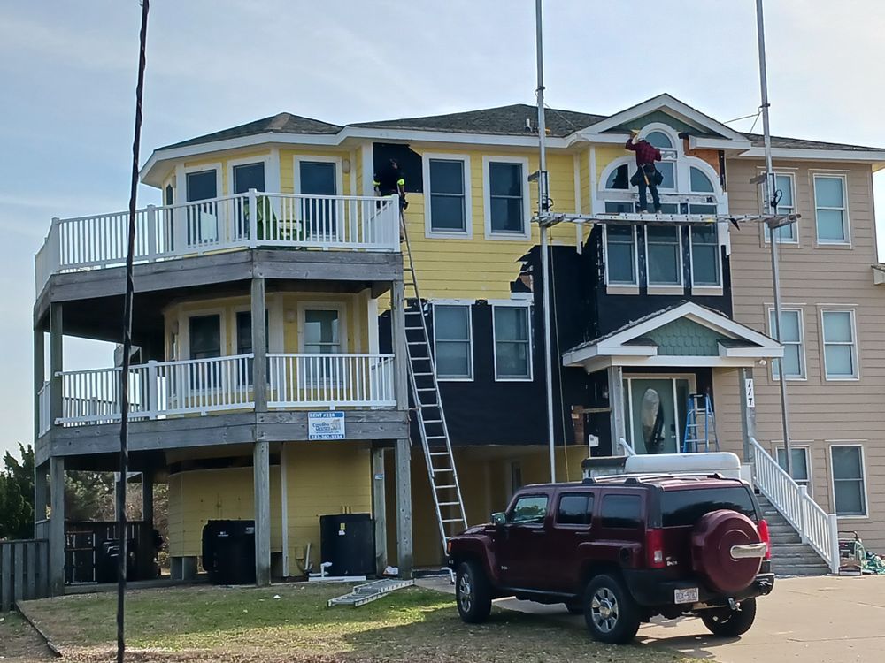 Yellow beach house with white balconies, a ladder, and a red SUV parked in front