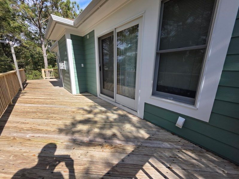 Wooden deck beside green house with sliding glass door and large windows in sunlight