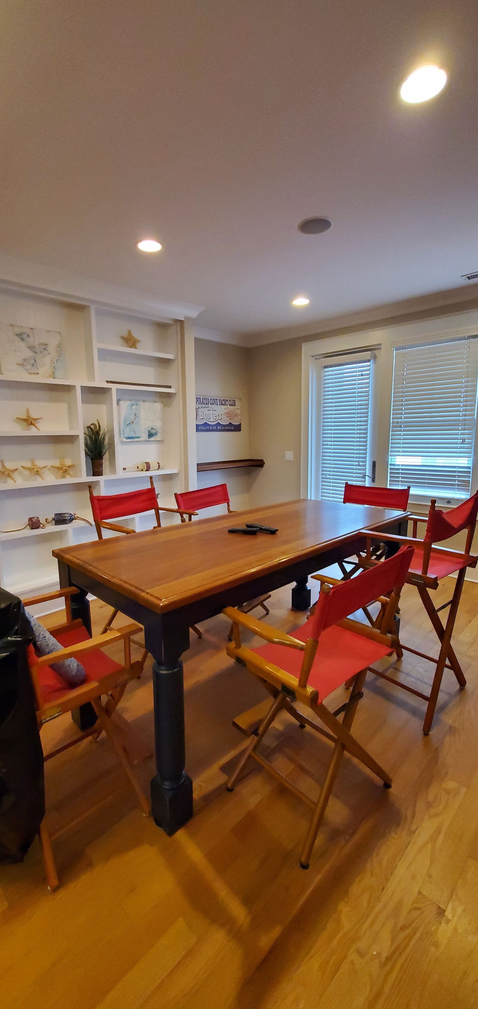 Bright dining room with a wooden table, red folding chairs, white shelves, and a window