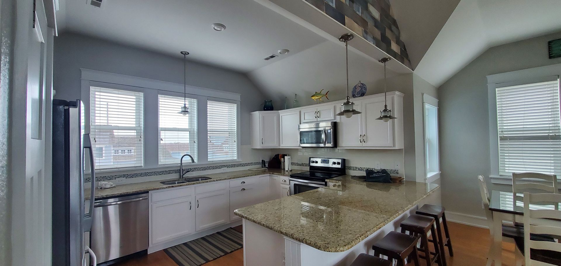 Bright kitchen with granite island, white cabinets, stainless appliances, and large windows by the sink.