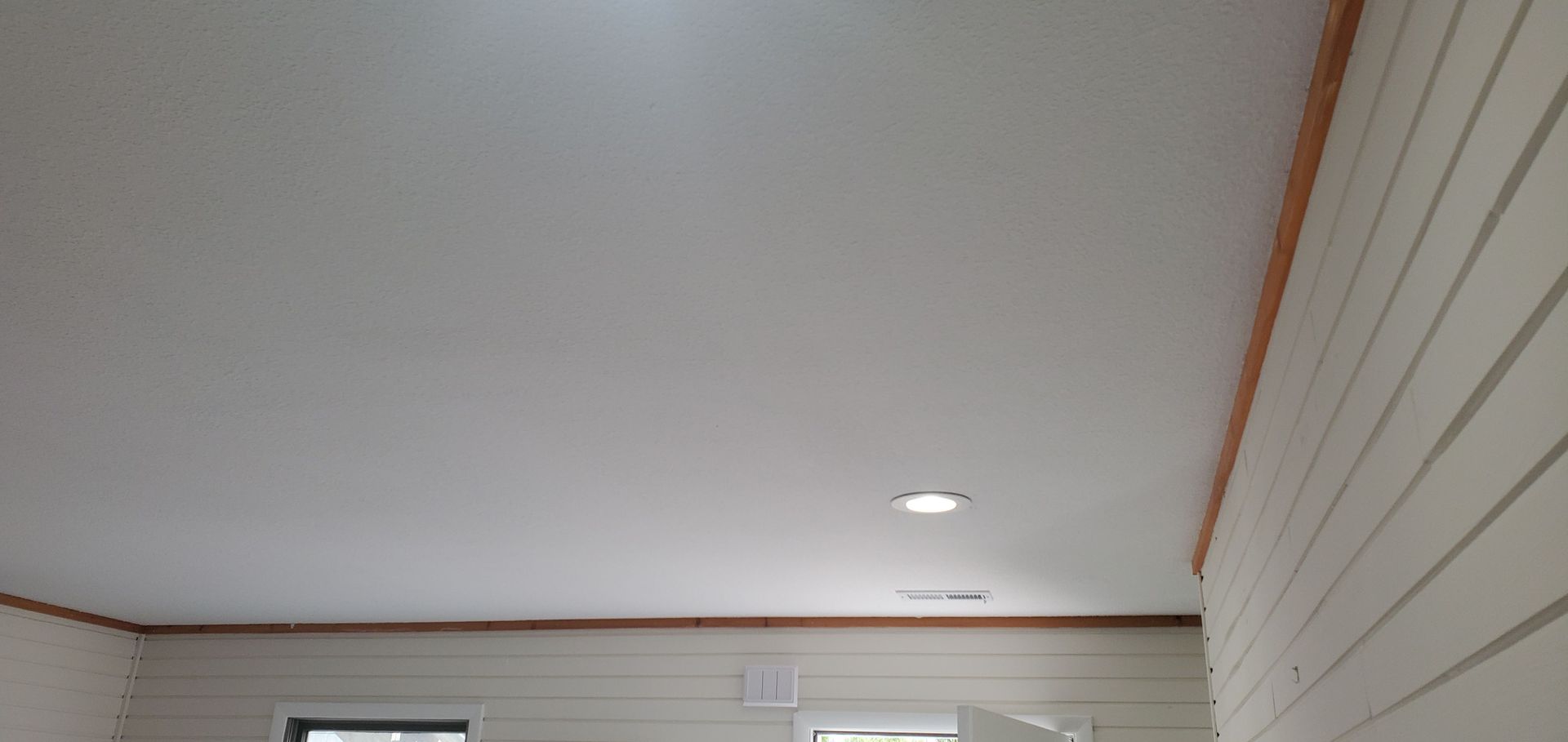 White ceiling with recessed light in a room, with wood trim and wall panels visible.