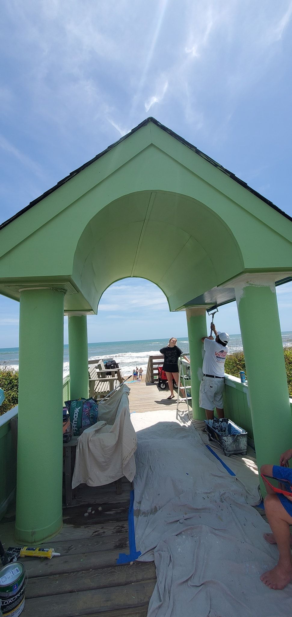 Green beach pavilion with columns, sandy path, and ocean view under a blue sky