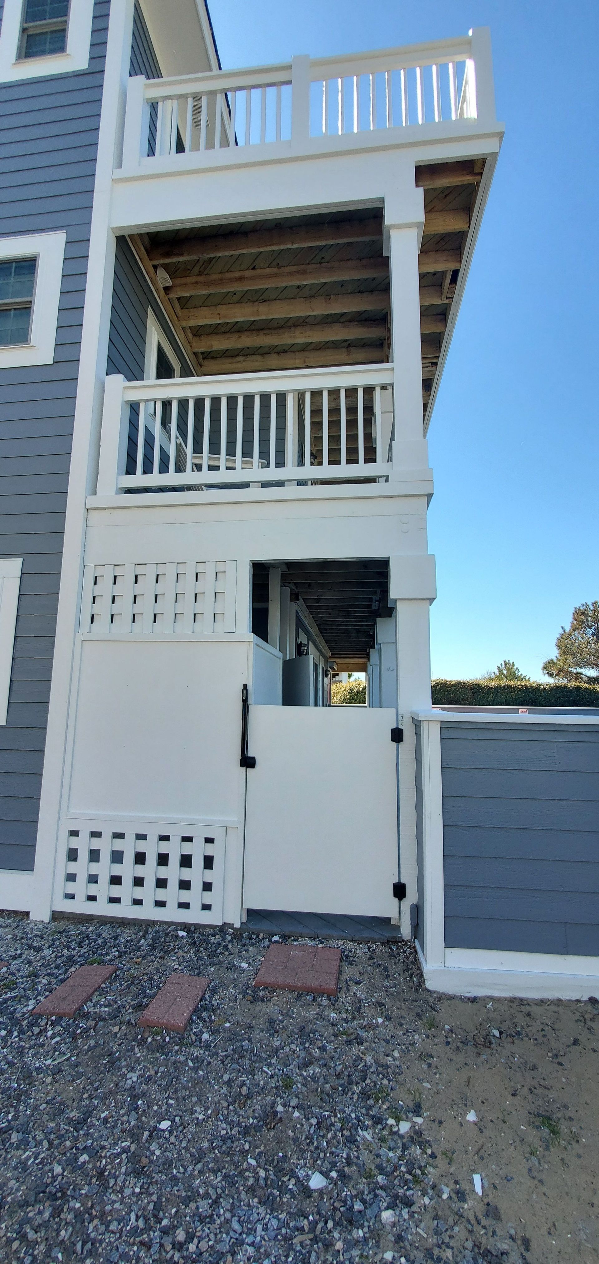 White multi-level outdoor stair tower and deck beside a gray fence under a clear blue sky