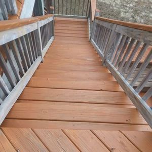 Wooden walkway with gray railings leading up to a doorway through a fenced outdoor structure