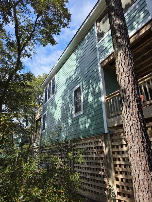 Side view of a light blue house with white trim and lattice skirting among tall trees.