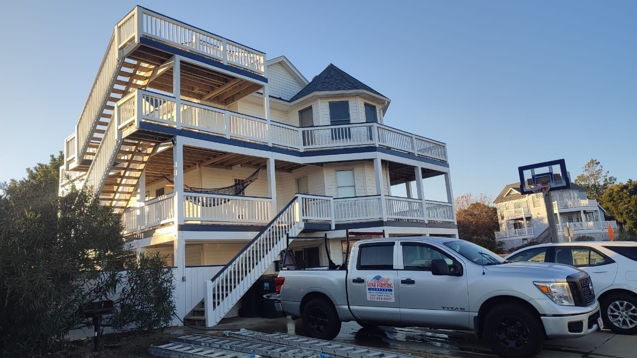 Three-story beach house with wraparound decks and parked white SUV in front at sunset