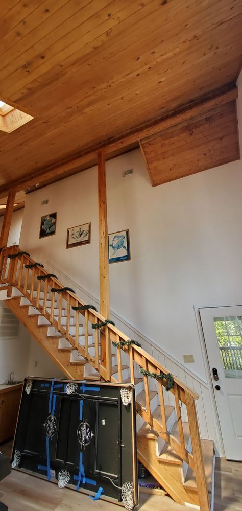 Wooden staircase in a lofted room with high wood ceiling, white walls, and black cabinets below.