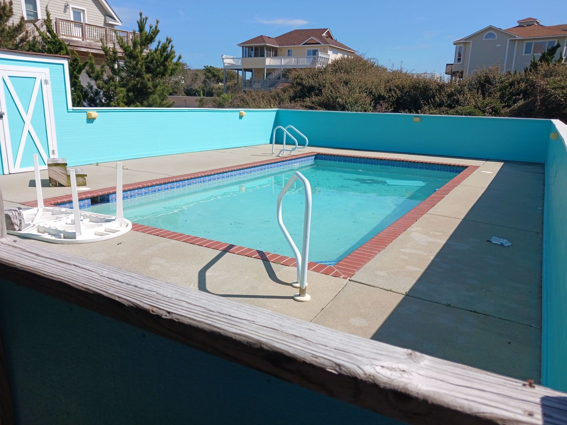 Small outdoor swimming pool with blue water, white rails, and a concrete deck under a clear sky.