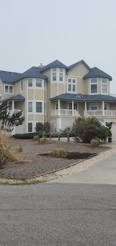 Large beige house with wraparound porch and landscaped front yard on a cloudy day