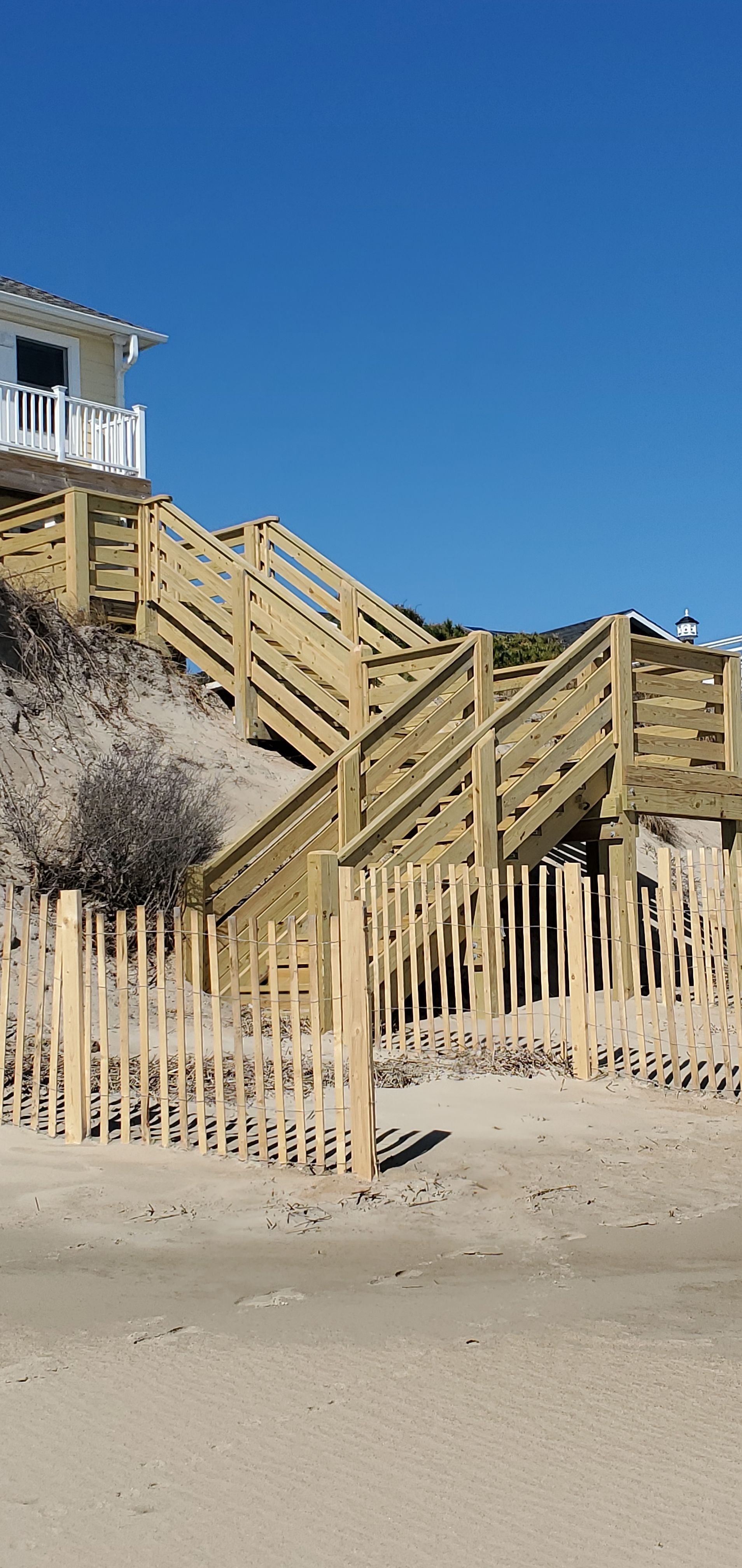 Wooden beach stairs and railings on a sandy dune under a clear blue sky