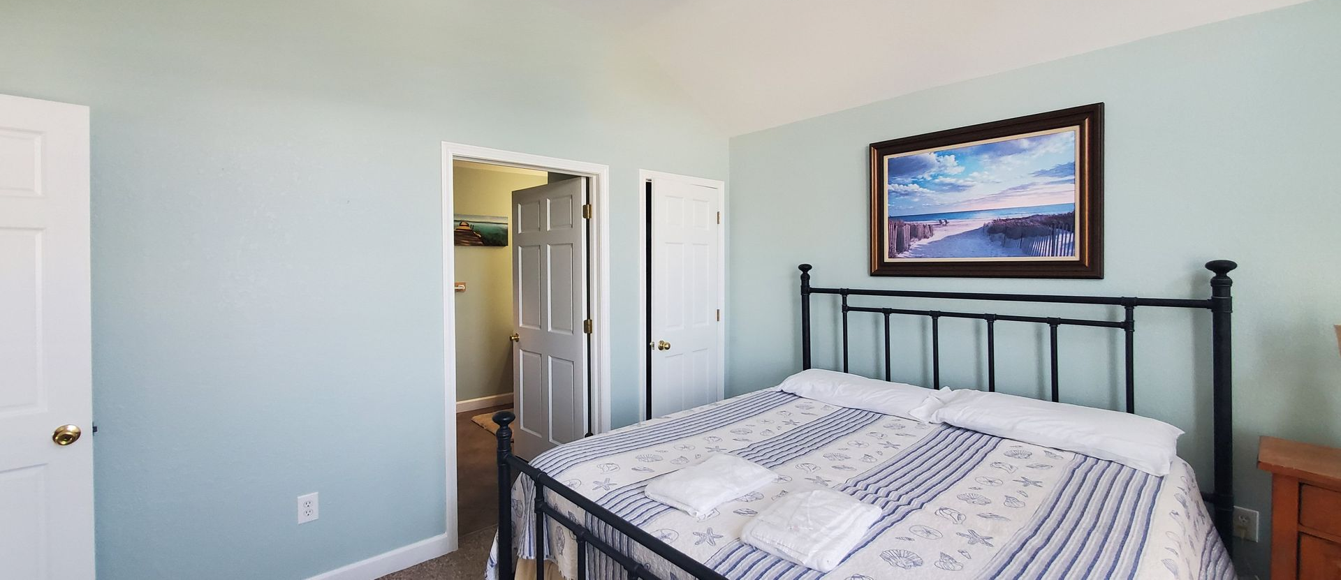 Small bedroom with a bed, open closet, white walls, and a framed landscape above the headboard.