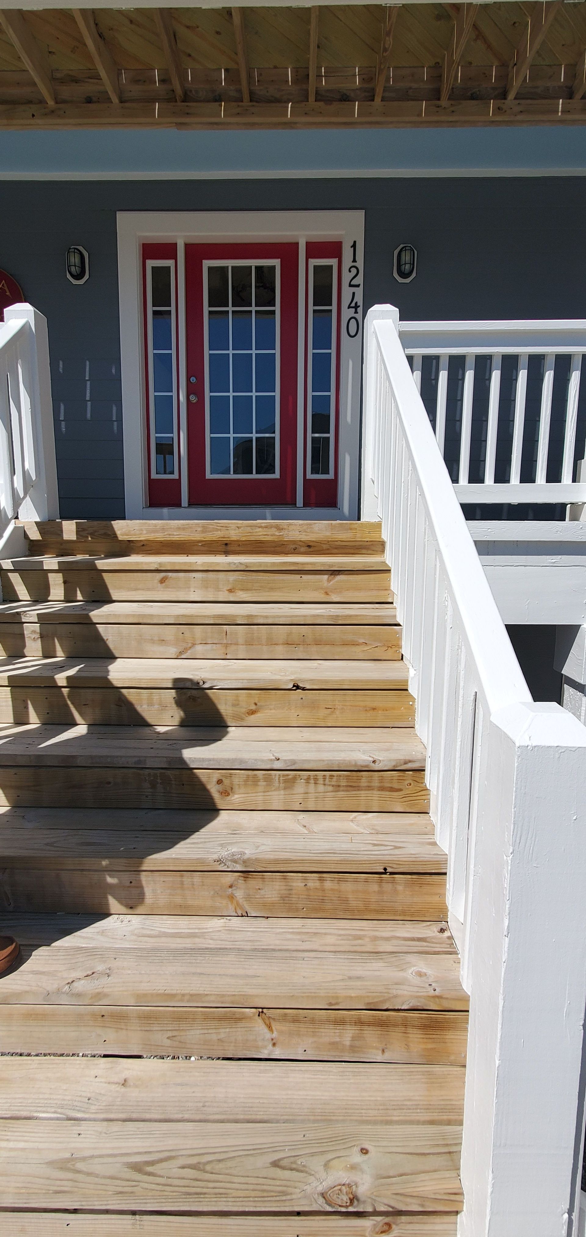 Wooden steps leading to red double doors with white railings and a porch