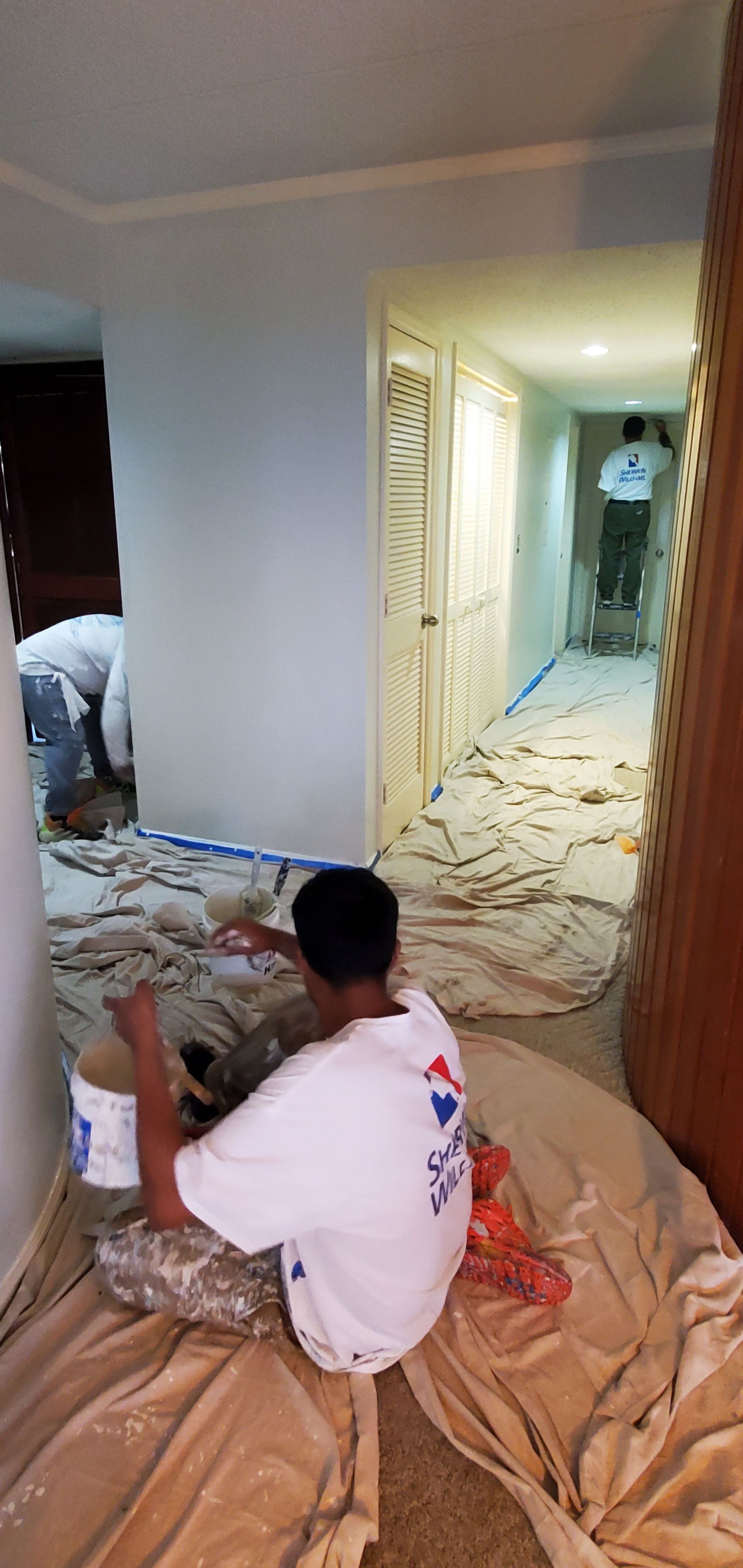 Two workers cover a hallway and floor with protective plastic during home renovation.