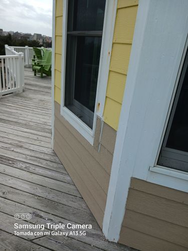 Deck beside yellow house with white railing and green chairs, viewed along the exterior wall.